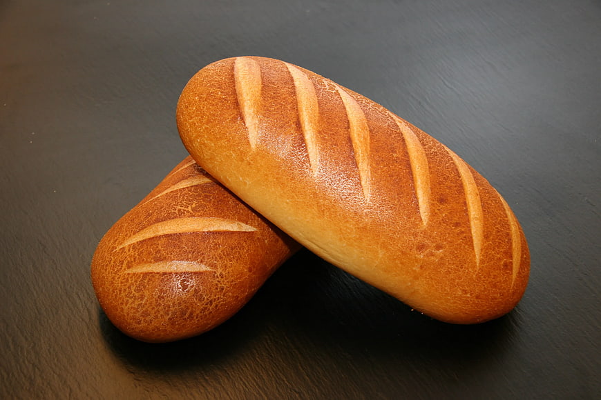 Two Golden Brown Loaves of Bread on Dark Slate