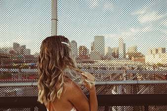 Woman with wavy hair looking at city skyline through fence