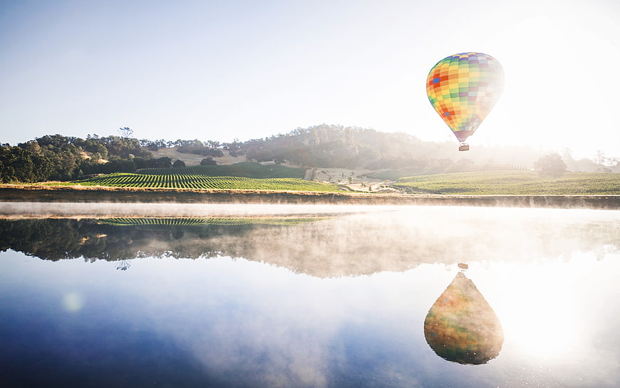Colorful hot air balloon reflecting in misty lake at sunrise