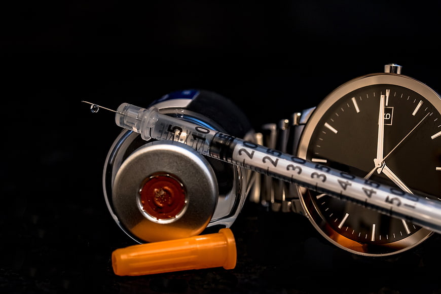 Insulin syringe and vial with wristwatch on black background