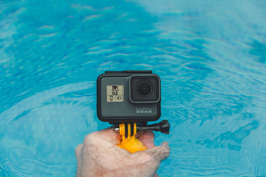 Hand holding GoPro camera over blue swimming pool water