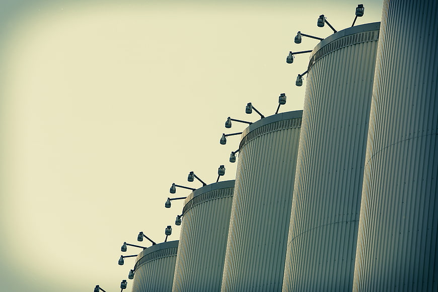 Row of industrial silos with floodlights against sky