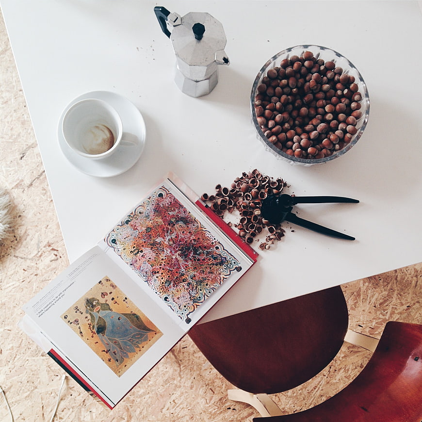 Flat lay of hazelnuts, coffee, and art book on white table
