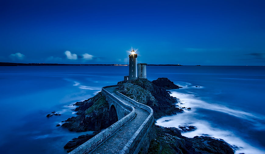 Lighthouse on rocky island at blue hour with long exposure waves