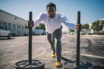 Athletic man pushing weighted sled in parking lot