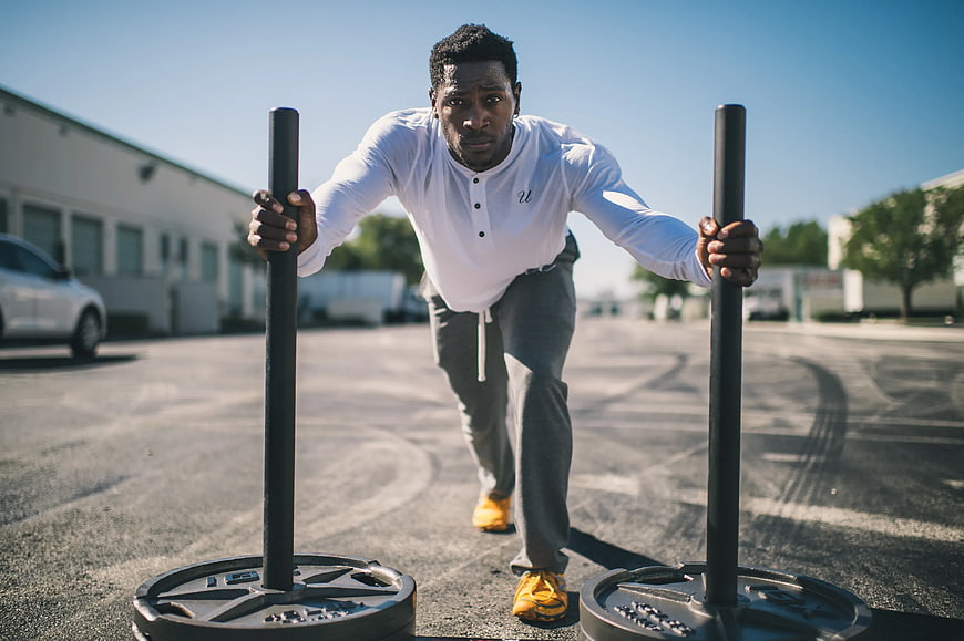 Athletic man pushing weighted sled in parking lot