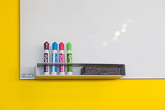 Whiteboard with colorful markers and eraser on yellow wall