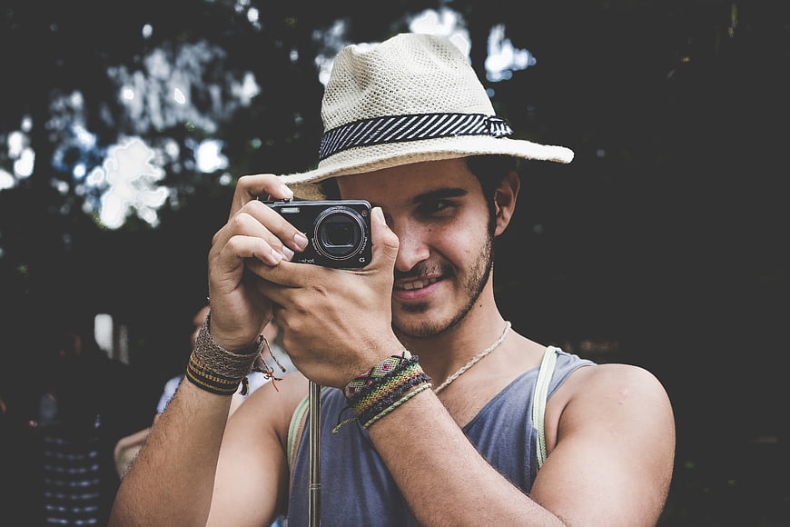 Young man with straw hat taking photo with digital camera