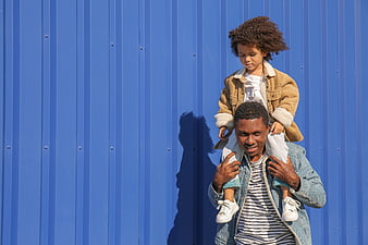 Father carrying child on shoulders against blue wall