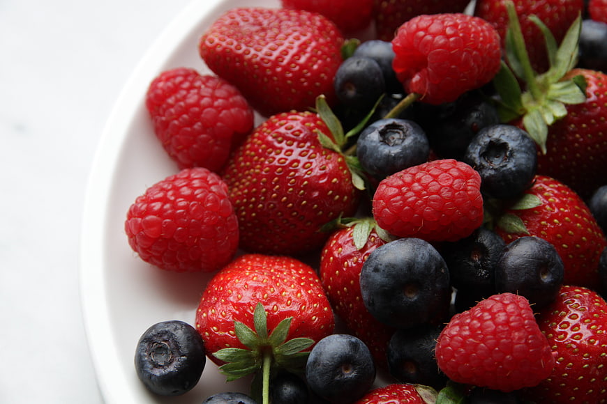 Close-up of fresh strawberries, raspberries, and blueberries on a white plate