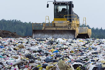Yellow bulldozer compacting waste at a landfill site