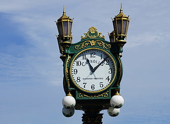 Vintage ornate street clock with green and gold details against blue sky