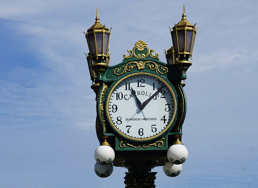 Vintage ornate street clock with green and gold details against blue sky