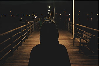 Silhouette of person in hoodie on pier at night