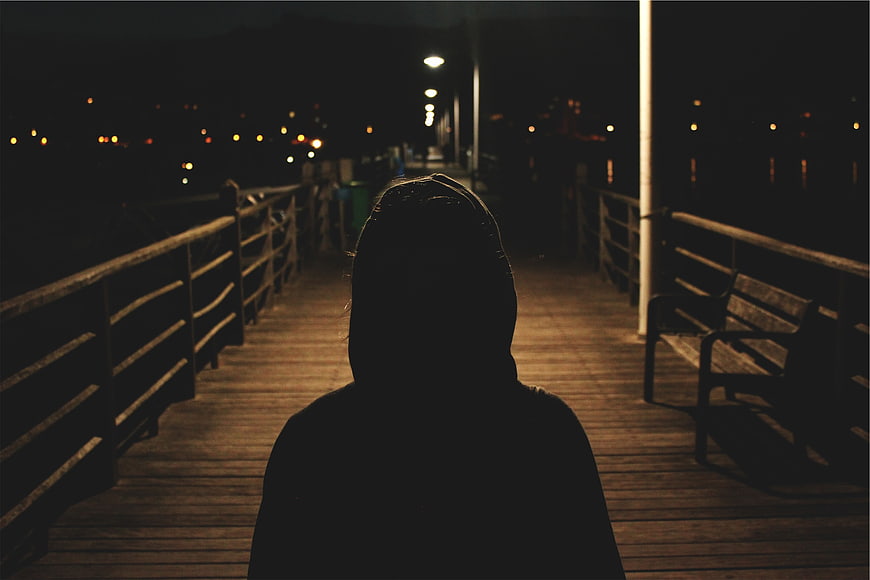 Silhouette of person in hoodie on pier at night