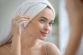 Woman applying serum with dropper in bathroom mirror