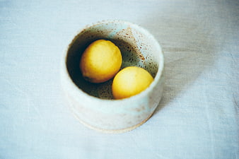 Two yellow lemons in a speckled ceramic bowl on linen