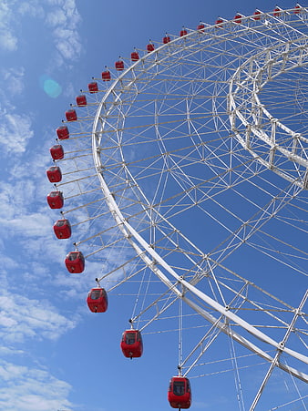 Red Ferris Wheel Against Blue Sky with White Clouds