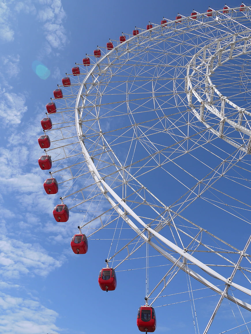 Red Ferris Wheel Against Blue Sky with White Clouds