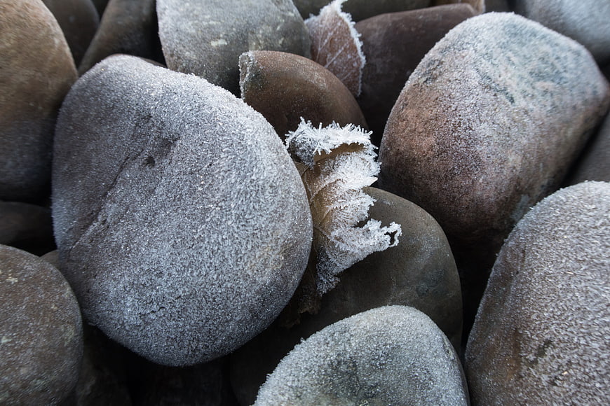 Close-up of frost-covered stones and frozen leaf in winter