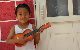 Young boy holding a small guitar against a red wall