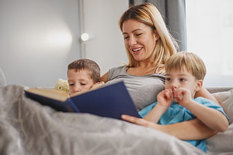 Mother reading book to two young boys on couch