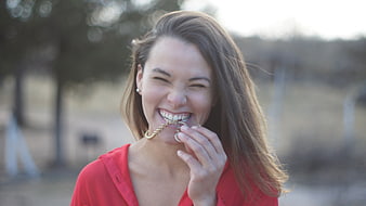 Joyful young woman biting gold chain outdoors