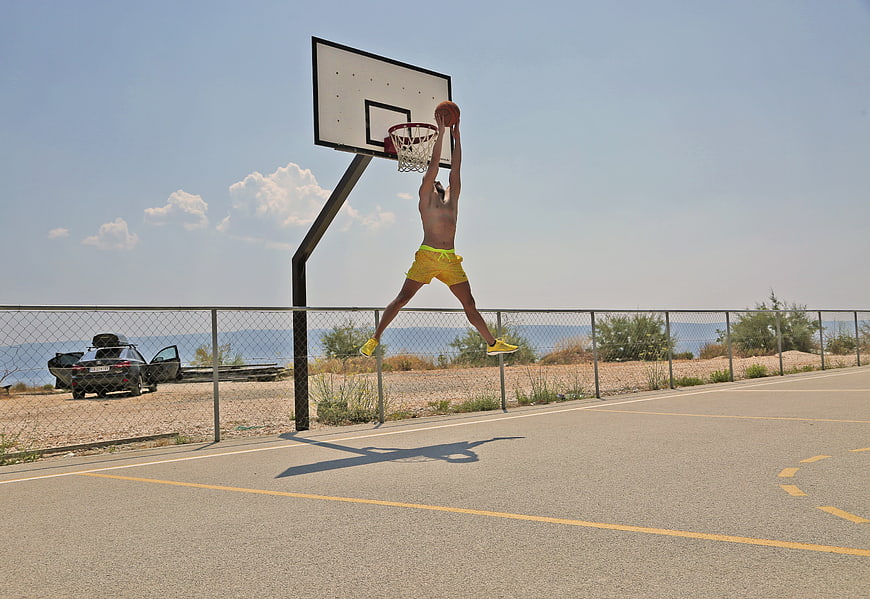 Male Athlete Dunking Basketball On Outdoor Court Near Beach