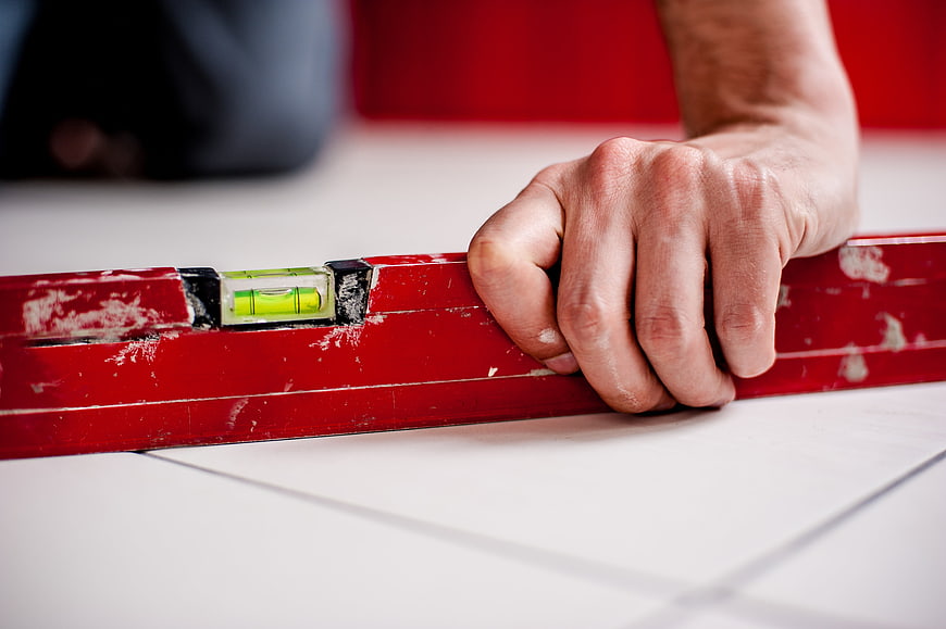 Hand holding red spirit level on white tiles