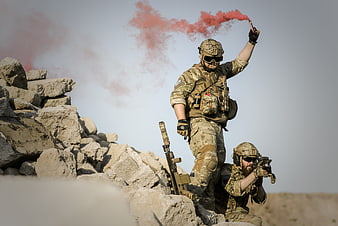 Soldiers in desert terrain with red smoke flare