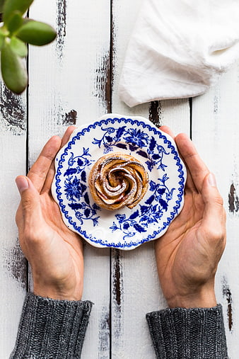 Hands holding cinnamon roll on blue floral plate
