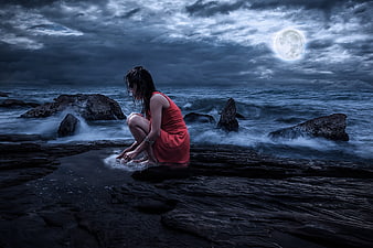 Woman in Red Dress Sitting on Rocks by Moonlit Sea