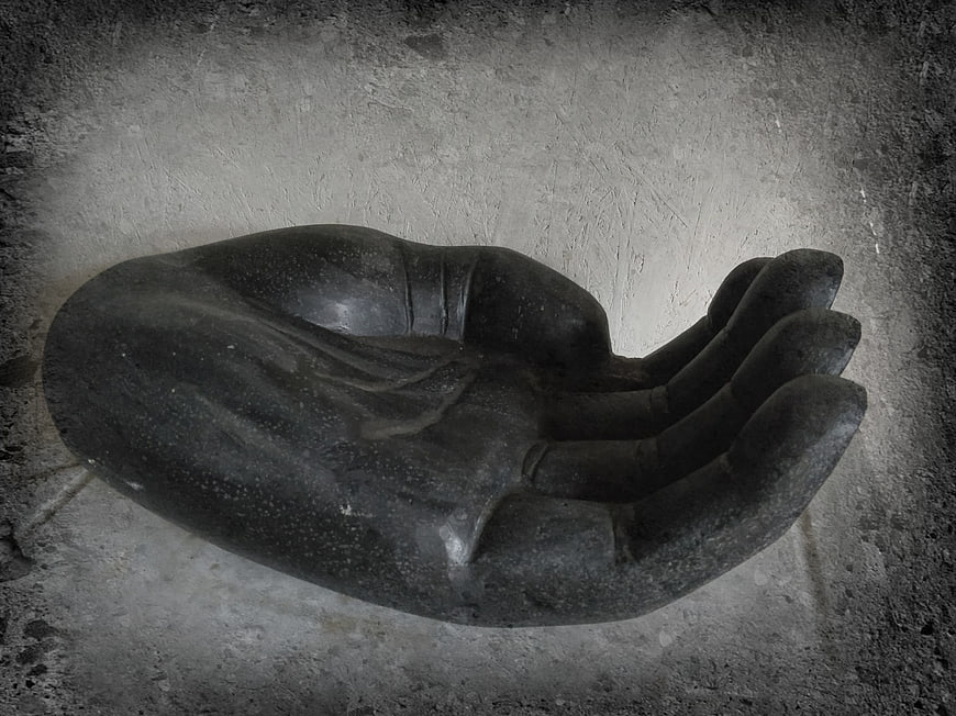 Black stone hand sculpture on textured concrete wall