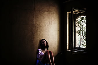 Lonely girl sitting in dark room by window