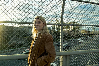 Blonde Woman in Brown Jacket Standing by Chain Link Fence