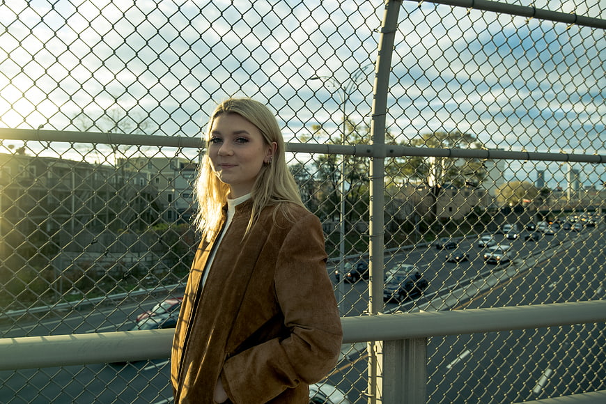 Blonde Woman in Brown Jacket Standing by Chain Link Fence