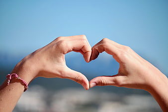 Hands forming heart shape against blue sky background