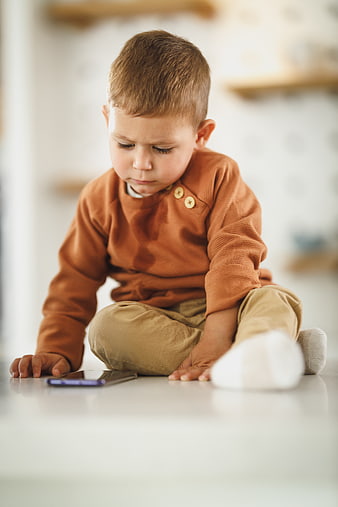 Toddler boy sitting on floor looking at smartphone