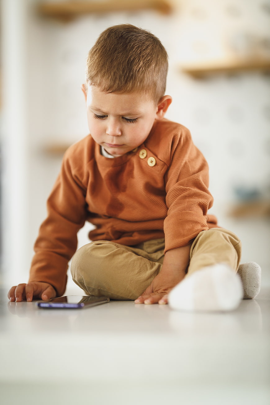 Toddler boy sitting on floor looking at smartphone