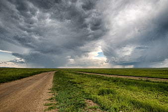 Dramatic Storm Clouds Over Vast Green Meadow and Dirt Road