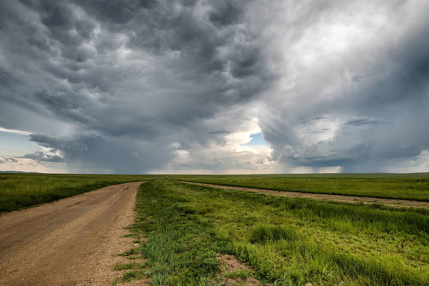Dramatic Storm Clouds Over Vast Green Meadow and Dirt Road