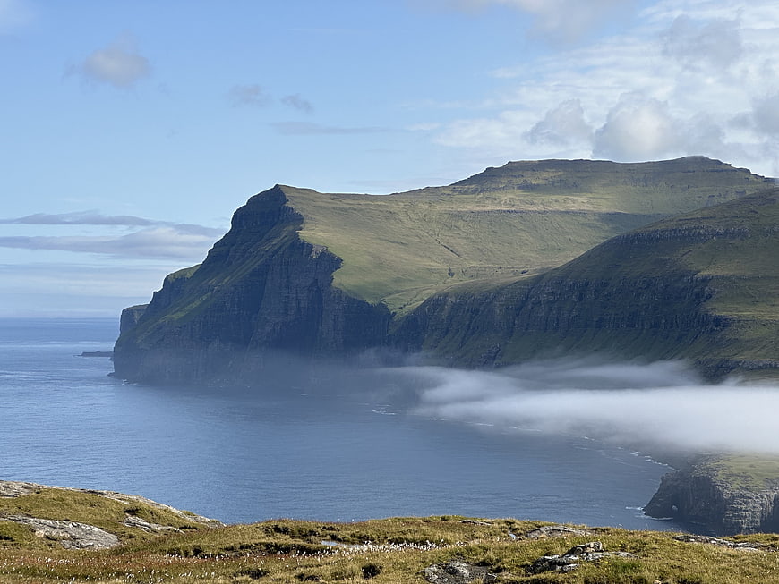 Dramatic coastal cliffs with low-lying fog and green mountains