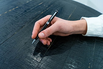 Hand holding black pen on dark wooden table