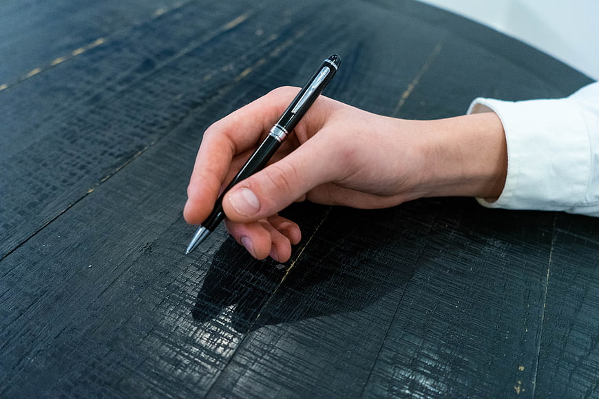 Hand holding black pen on dark wooden table