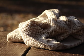 Cozy beige knitted sweater on wooden surface in sunlight