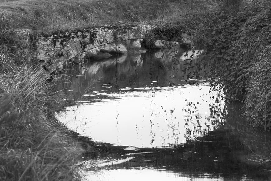 Black and white photo of a small stone bridge over a stream