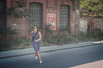Woman jogging on street past abandoned brick building