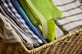 Woven basket filled with colorful dish towels and a green scrub brush
