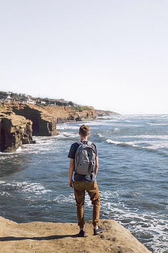 Man with Backpack Standing on Cliff Overlooking Ocean