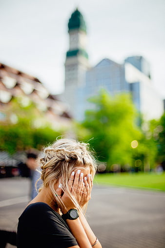 Blonde woman covering face with hands in city park
